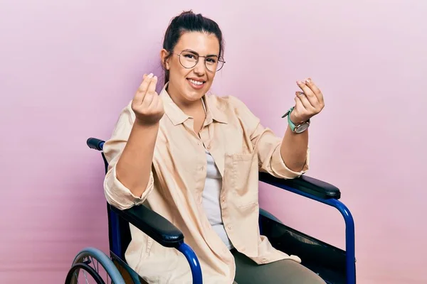 車椅子の若い女性が手で金のジェスチャーをして給料支払いや億万長者のビジネスを求めています — ストック写真