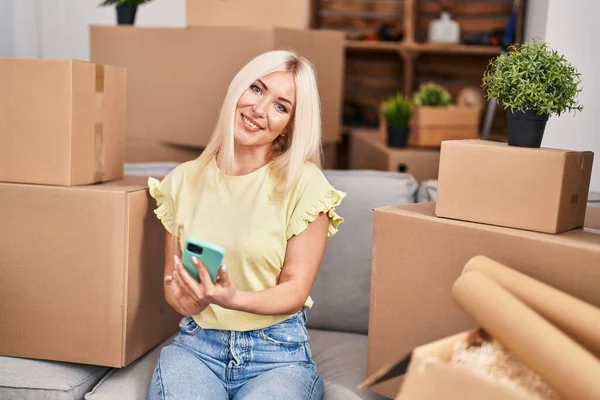 Genç sarışın kadın akıllı telefon kullanıyor. Yeni evinde yerde oturuyor.