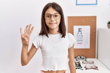 Young hispanic girl wearing glasses showing and pointing up with fingers number four while smiling confident and happy. 