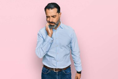 Sakallı, iş gömleği giyen orta yaşlı bir adam diş ağrısı ya da diş hastalığından dolayı acı dolu bir ifadeyle ağıza dokunuyor. dişçi 