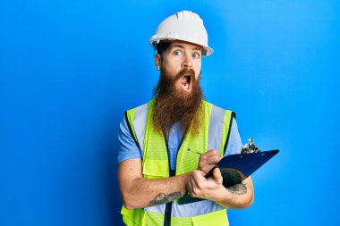 Uzun sakallı, güvenlik kaskı takan, şok suratlı, şüpheli ve alaycı bakışlı, ağzı açık bir şekilde şaşırmış bir adam. 