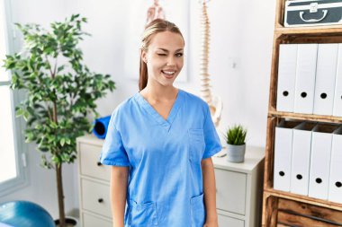 Ağrı kesici kliniğinde çalışan beyaz bir kadın kameraya seksi bir ifadeyle bakıyor, neşeli ve mutlu bir yüzle.. 