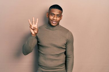 Balıkçı yaka kazak giyen genç siyahi bir adam üç numaralı parmaklarıyla kendini beğenmiş ve mutlu gülümserken onu işaret ediyor.. 