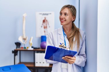 Fizyoterapi kliniğinde kontrol listesine yazılı fizyoterpist üniforması giyen genç sarışın kadın.