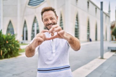 Şehirdeki orta yaşlı adam aşka gülümseyip elleriyle kalp sembolü çiziyor. romantik kavram. 