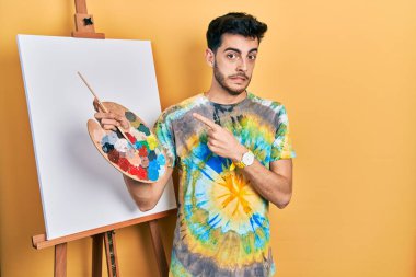 İspanyol asıllı genç adam paletle resim çiziyor. Resim sehpası kenara çekilip endişeli ve endişeli bir ifade sergiliyor. 