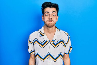 Günlük kıyafetler giyen genç İspanyol adam komik yüzlü yanakları şişiriyor. Havayla şişmiş ağız, çılgın bir ifade.. 