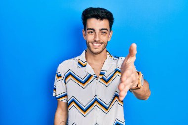 Gündelik kıyafetler giyen genç İspanyol adam dostça bir selamlama ve hoş geldin hediyesi olarak el sıkışmayı sunuyor. başarılı iş. 