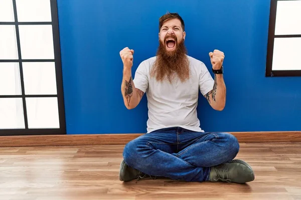 Redhead Man Long Beard Sitting Floor Empty Room Celebrating Surprised — Stockfoto