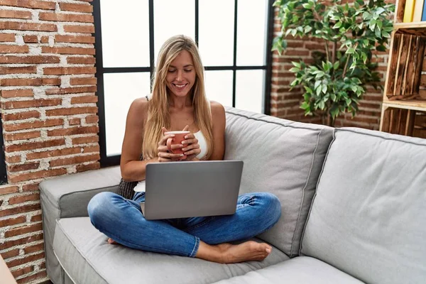 Νεαρή Ξανθιά Γυναίκα Που Χρησιμοποιεί Φορητό Υπολογιστή Και Πίνει Καφέ — Φωτογραφία Αρχείου