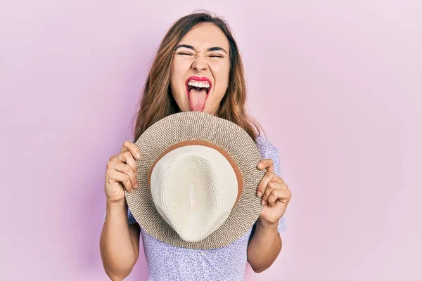 Young Hispanic Girl Wearing Summer Hat Covering Mouth Sticking Tongue — Stockfoto