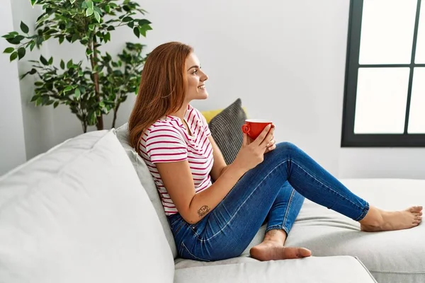 Evdeki kanepede kahve içen genç bir kadın.