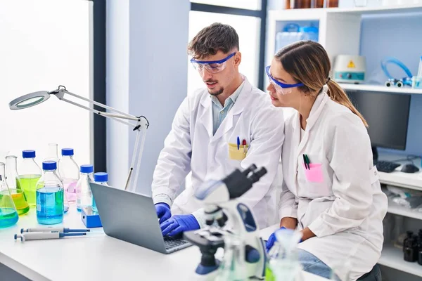 Genç erkek ve kadın bilim adamları laboratuarda çalışan dizüstü bilgisayarlarını kullanıyorlar.