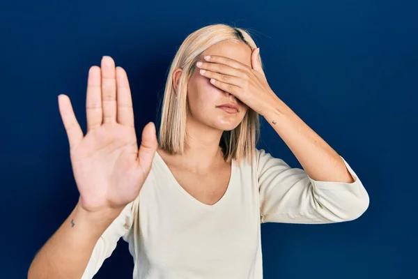 Beautiful blonde woman wearing casual sweater covering eyes with hands and doing stop gesture with sad and fear expression. embarrassed and negative concept.