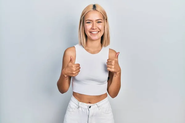 Beautiful blonde woman wearing casual style with sleeveless shirt success sign doing positive gesture with hand, thumbs up smiling and happy. cheerful expression and winner gesture.
