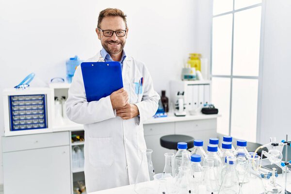 Middle age hispanic man smiling confident wearing scientist uniform at laboratory