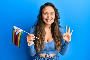 Zimbabwe bayrağı tutan genç İspanyol kız parmaklarıyla imza atıyor, gülümseyerek mükemmel bir sembol oluşturuyor. 