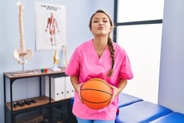 Fizyoterapi kliniğinde çalışan genç İspanyol bir kadın basketbol topu tutuyor ve kameraya bakıp öpüşürken çok güzel ve seksi oluyor. aşk ifadesi. 