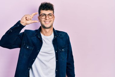 Günlük kıyafetler giyen, gözlüklü, gülümseyen, kendine güvenen, el hareketi yapan, parmaklarıyla işaret yapan ve kameraya bakan genç İspanyol bir adam. ölçüm kavramı. 