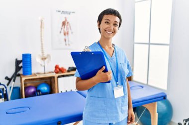 Kısa saçlı, İspanyol bir kadın. Ağrı kesici kliniğinde çalışıyor. Yüzünde mutlu ve havalı bir gülümseme var. şanslı kişi. 