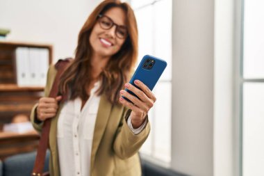 Klinikte akıllı telefon kullanan kendine güvenen genç Latin kadın.