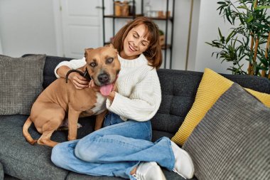 Beyaz bir kadın gülümsüyor. Kendine güvenen bir köpek. Evdeki kanepede oturuyor.