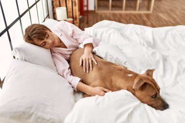 Beyaz bir kadın yatak odasında köpekle yatakta yatıyor.