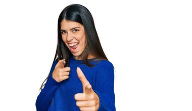 Gündelik kıyafetler giyen genç İspanyol kadın mutlu ve komik yüzüyle kamerayı işaret ediyor. iyi enerji ve titreşimler. 