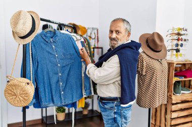 Kıdemli gri saçlı adam elbise mağazasında akıllı telefon kullanarak fotoğraf çekiyor.