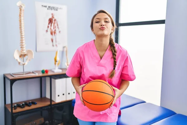 バスケットボールボールを持った理学療法クリニックで働く若いヒスパニック系の女性がカメラを見てキスが可愛くてセクシーさを吹いています 愛の表現 — ストック写真