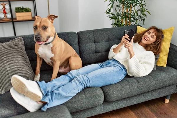 家で犬とソファに横たわっスマートフォンを使用して若い白人女性 — ストック写真