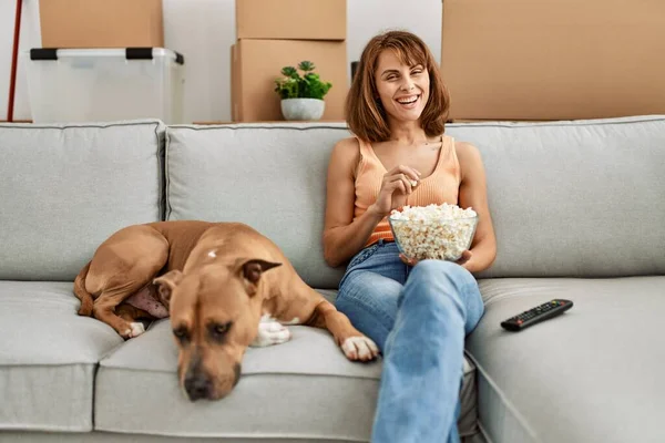 Young caucasian woman watching movie sitting on sofa with dog at home