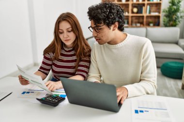 Ciddi ifadeleri olan genç bir çift evde masada dizüstü bilgisayar kullanıyor..
