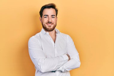 Beyaz iş gömleği giyen, kollarını kavuşturup kameraya gülümseyen yakışıklı, beyaz sakallı bir adam. pozitif kişi. 