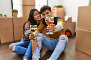 Genç Latin çift yeni evlerinde yerde oturmuş şarapla kadeh kaldırıyor..