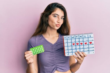 Elinde doğum kontrol hapları ve regl takvimi olan beyaz bir kadın kameraya bakıp öpüşüyor ve çok seksi oluyor. aşk ifadesi. 