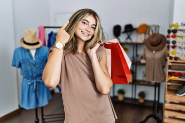 Alışveriş poşetleri taşıyan genç sarışın kadın tek parmağıyla başını gösteren gülümseme, harika bir fikir ya da düşünce, iyi bir hafıza. 