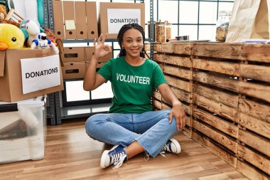 Young african american woman wearing volunteer t shirt at donations stand smiling positive doing ok sign with hand and fingers. successful expression. 