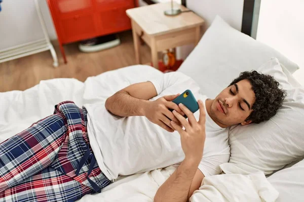 Junger Hispanischer Mann Mit Smartphone Auf Dem Bett Schlafzimmer Liegend — Stockfoto