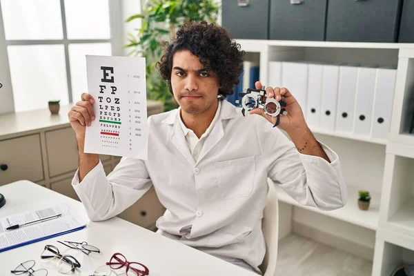 头发卷曲的西班牙裔男人拿着验光眼镜 视力测试有疑问 神经紧张 因为问题皱着眉头 消极的人 — 图库照片