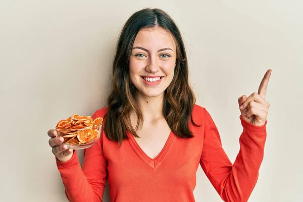 Joven Morena Sosteniendo Tazón Naranja Seca Sonriendo Feliz Señalando Con —  Fotos de Stock