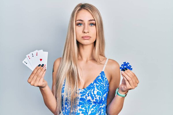 Young beautiful caucasian woman holding poker cards and chips relaxed with serious expression on face. simple and natural looking at the camera. 