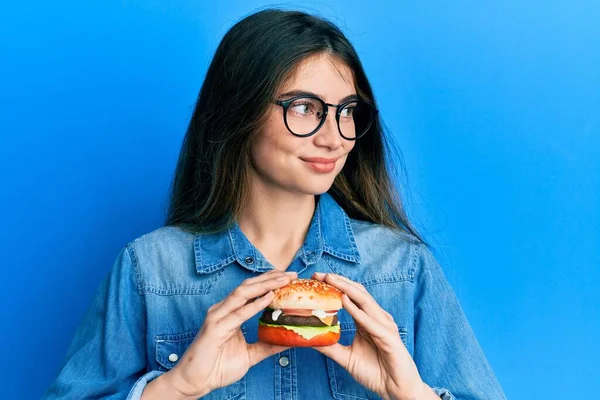 Young Caucasian Woman Eating Tasty Classic Burger Smiling Looking Side — Stock fotografie