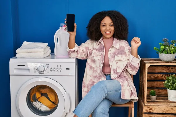 Young African American Woman Doing Laundry Using Smartphone Screaming Proud — Stockfoto