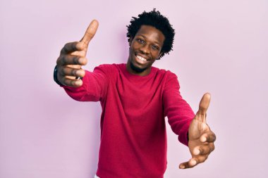 Gündelik giysiler giymiş genç Afro-Amerikan bir adam kameraya sarılıp gülümseyerek bakıyor. Mutluluğu kucaklayan neşeli bir ifade.. 