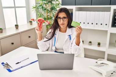 Genç İspanyol doktor kadın anatomik kadın organı ve doğum kontrol hapları tutuyor. Depresyonda ve endişe içinde, sinirli ve korkmuş. hüzünlü ifade. 