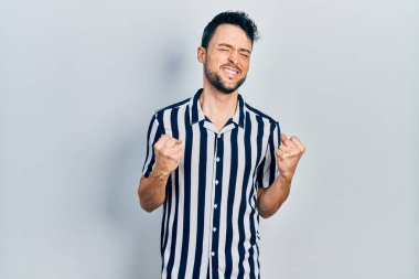 Gündelik kıyafetler giyen genç İspanyol adam başarı için heyecanlı kolları havada ve gözleri kapalı zaferi kutlarken gülümsüyor. Kazanan konsept. 