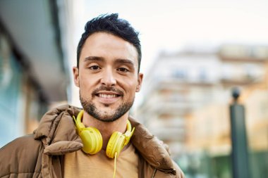 Şehirde kulaklık takarak mutlu gülümseyen genç İspanyol adam..