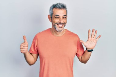 Yakışıklı, orta yaşlı, gri saçlı, sıradan tişörtlü, altı numaralı parmaklarını gösterip gülümseyen, kendinden emin ve mutlu bir adam.. 