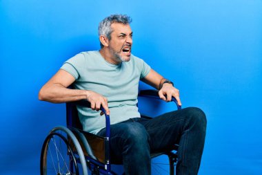 Yakışıklı, orta yaşlı, gri saçlı, tekerlekli sandalyede oturan sinirli ve kızgın bir şekilde bağıran öfkeli bir adam. Öfkeyle bağırıyor. öfke ve agresif konsept. 